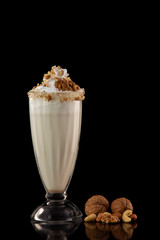 Glass of sweet milkshake with nuts isolated at black background.