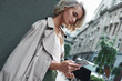 Fashion. Young stylish woman standing on the city street using application on smartphone concentrated close-up