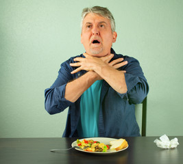 A man is panicking and is in trouble as he chokes on food and is making the official international sign for 