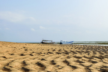 Sanur beach during low tides time of Indian ocean in Bali with two boats in background