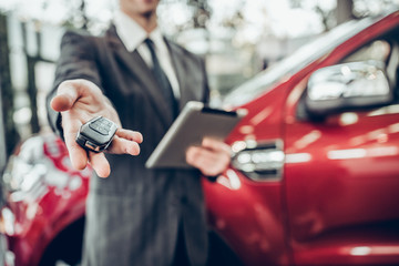 Wall Mural - Man in suit offering a car key to the observer, with a car in the background