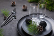 Dark christmas table setting design. Black  plates, champagne glasses, fork and knife set with napkin, fir branch, christmas decorations