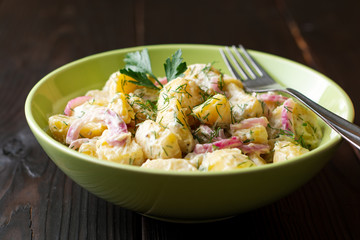 Wall Mural - Potato salad with red onion and greens in bowl on dark wooden table. Selective focus.