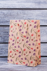 Large paper shopping bag with a pattern of flowers. Tulips pattern paper gift bag on wooden background. Womens Day sale concept.