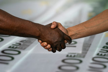 African And European Handshake As A Sign Of Friendship, Greeting, Agreement Or Deal,against The Background Of 100 Euro Banknotes.
