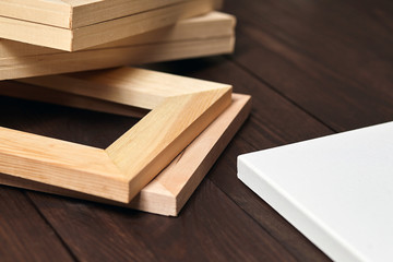 Pile of wooden stretchers and a white blank artistic cotton canvas lying on a dark brown table