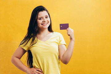 Portrait of a happy young girl showing plastic credit card isolated over yellow background