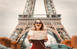 © Masson - Style redhead girl in red coat and bag with map in parisian park in autumn season time. Eiffel tower on background