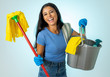Young attractive woman holding cleaning tools and products in bucket isolated on blue background