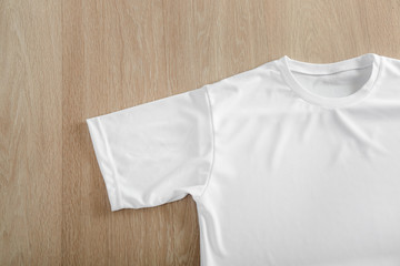 White t-shirt on wooden background, top view