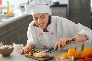 Young female chef putting tasty dish onto wooden board on kitchen table