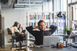 © Maskot - Businessman sitting with hands behind head at desk in office