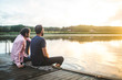 © Maskot - Friends looking at lake while sitting on dock during sunset