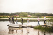 © Maskot - Male and female friends enjoying on jetty over lake against clear sky during weekend getaway