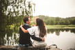 © Maskot - Rear view of romantic couple sitting on retaining wall against lake