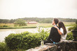 © Maskot - Couple looking at lake while sitting on retaining wall