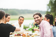 © Maskot - Portrait of smiling young man enjoying dinner with friends at table in backyard