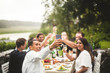 © Maskot - Man taking selfie with friends holding drinks during dinner party in backyard