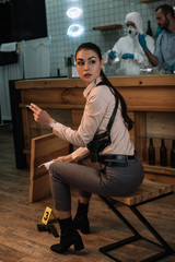 Wall Mural - cropped view of smoking female detective sitting at crime scene with colleagues working behind