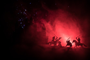 Medieval battle scene with cavalry and infantry. Silhouettes of figures as separate objects, fight between warriors on dark toned foggy background with medieval castle. Night scene. Selective focus