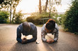 © Maskot - Athletes doing plank exercise on road in park during sunset