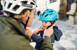 © Halfpoint - A young father putting on a helmet on his toddler son's head outdoors in city.