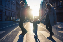 A Small Toddler Boy With Parents Crossing A Road Outdoors In City At Sunset.