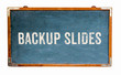 “Backup Slides” text word message written on a wide blue old grungy vintage wooden chalkboard or retro blackboard with frame isolated on white background.