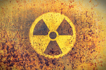 Wall Mural - Round yellow radioactive (ionizing radiation) danger symbol painted on a massive rusty metal wall with rustic grunge texture background. Washed fading yellow rust color toned.