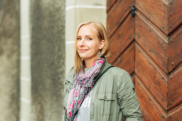 Outdoor portrait of beautiful blond woman, posing outdoors, wearing khaki color parka and pink scarf