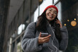 © Oleksii - Cheerful happy asian woman in stylish clothing, red hat and hipster eyeglasses listening music outdoors. Portrait of smiling Korean female walking on street, using mobile phone. Positive lifestyle.