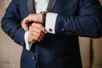 Wall Mural - Close-up man puts on a gold watch with a leather belt, businessman is dressed in a stylish suit, a white shirt.