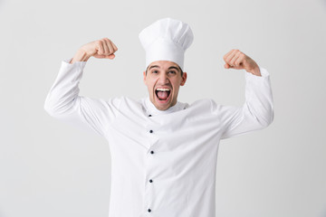 Wall Mural - Excited young man chef indoors isolated over white wall background showing biceps.