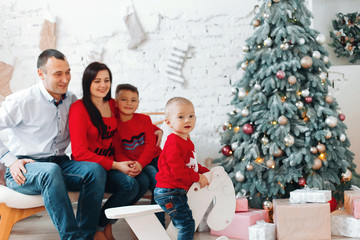 Happy Young Family With Two Children Holding Christmas Gift and Smiling at Camera Near Christmas tree. New Year Celebration. Decorations