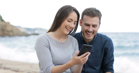 Wall Mural - Happy couple browsing smart phone content on the beach