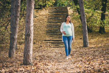 happy pregnant woman is walking in park.