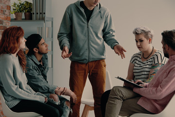 Wall Mural - Man speaking to group of young people with problems during therapy with psychologist