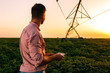 © Zoran Zeremski - Young farmer holding tablet in his hands and adjusts irrigation system on soybean field at sunset.