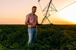 © Zoran Zeremski - Young farmer holding tablet in his hands and adjusts irrigation system on soybean field at sunset.