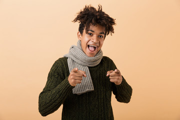 Poster - Portrait of joyous african american guy wearing sweater and scarf gesturing at camera, isolated over beige background