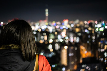 Young asian woman with short black hair is standing on a observation deck and looks at the night Tokyo (blurry background)