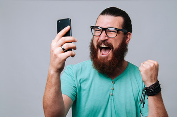 Bearded hipster man looking at phone and celebrating success