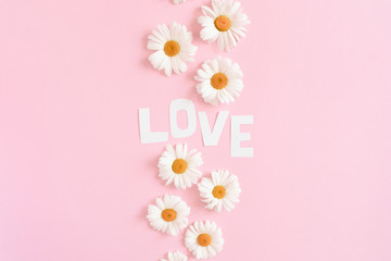 Wall Mural - Word Love made of letters cut out of paper. Pattern made of white chamomile on a pink pastel background