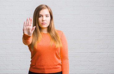 Sticker - Young adult woman over white brick wall with open hand doing stop sign with serious and confident expression, defense gesture