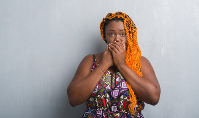 Canvas Print - Young african american woman over grey grunge wall wearing orange braids shocked covering mouth with hands for mistake. Secret concept.