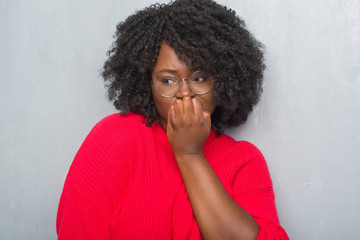 Sticker - Young african american woman over grey grunge wall wearing winter sweater and glasses looking stressed and nervous with hands on mouth biting nails. Anxiety problem.