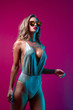 Hot woman in silver body suit with sunglasses on a purple magenta background with blue lights