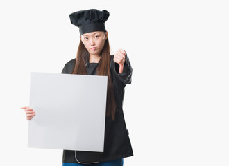 Sticker - Young Chinese woman over isolated background wearing chef uniform holding banner with angry face, negative sign showing dislike with thumbs down, rejection concept