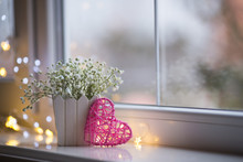 Pink Wicker Heart And Bouquet Of Beautiful White Gypsophila Near Window In The Daylight, Bokeh Lights On Background.