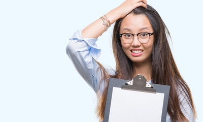 Sticker - Young asian business woman holding clipboard over isolated background stressed with hand on head, shocked with shame and surprise face, angry and frustrated. Fear and upset for mistake.